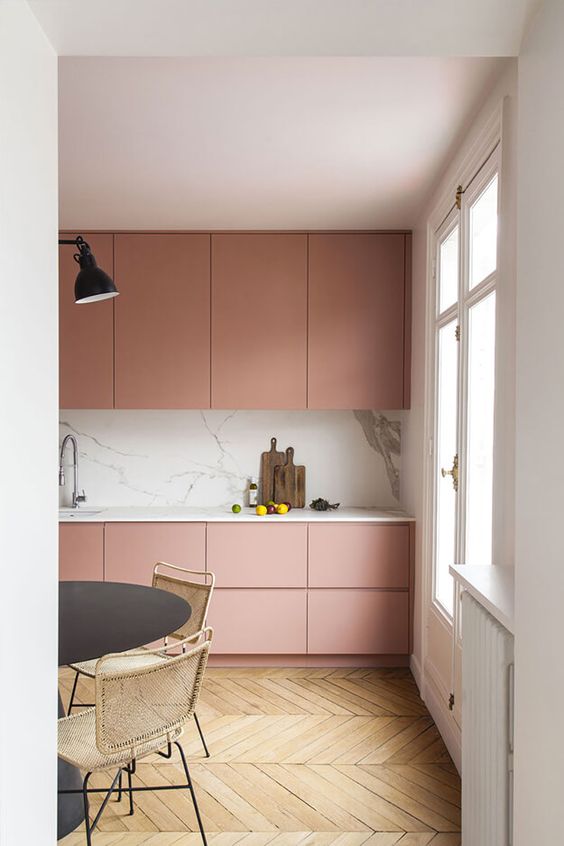a sophisticated, minimalist pink kitchen with an elegant white marble backsplash and worktop, a black table and woven chairs