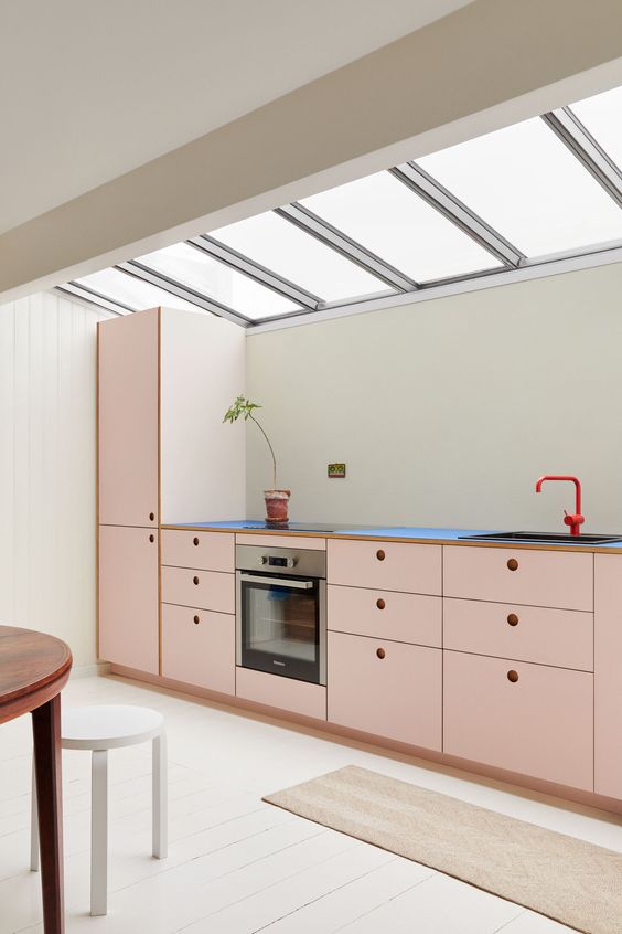A loft kitchen with blush MDF cabinets, black countertops, a red faucet, and lots of natural light is cool