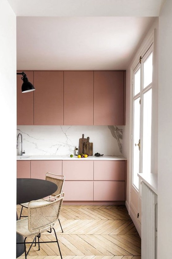 An ultra-minimal dusty pink kitchen with sleek cabinets, a white marble backsplash and countertops, and black accents