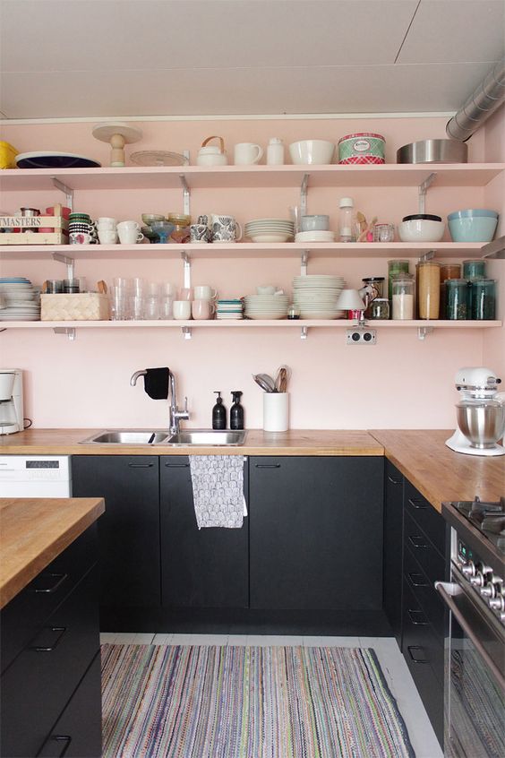 Blush walls and shelves contrast with the black cabinets, creating a chic and stylish color combination
