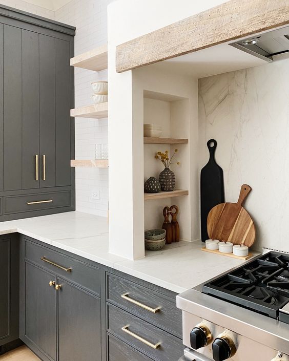A modern farmhouse kitchen with graphite gray cabinets, built-in cupboards and an alcove with small shelves used for storage and display