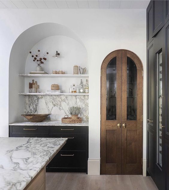 A modern kitchen with a large arched alcove with dark built-in cabinets, open shelving and a marble backsplash is charming
