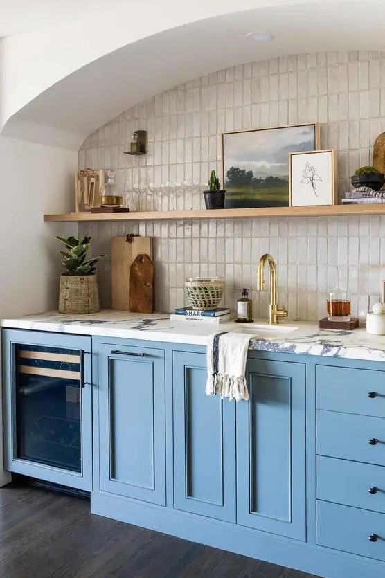 an arched niche lined with thin mother-of-pearl tiles, with an open shelf for displaying art and decor and blue cabinets