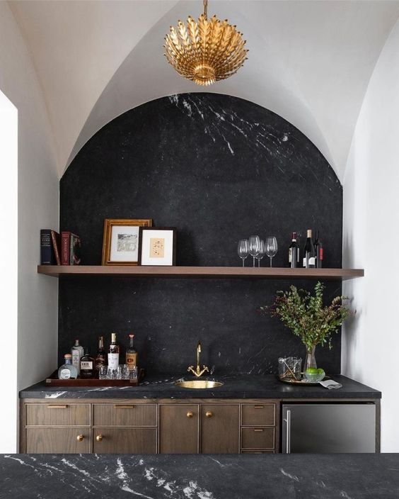 an exquisite kitchen with dark stained cabinets and a kitchen island, black marble countertops and a backsplash, an arched niche housing a portion of the cabinets