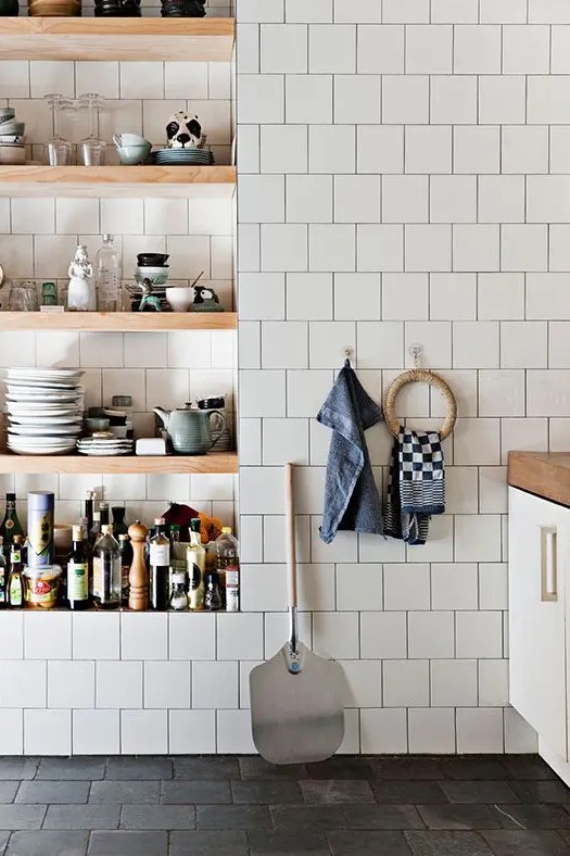 a kitchen covered in white square tiles and with niche shelves used instead of cabinets to store everything you need