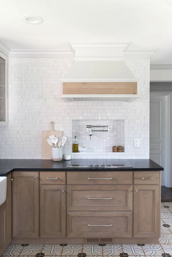 a farmhouse kitchen with stained cabinets, black countertops, white tiles, and a nook over the stove to store everything for cooking