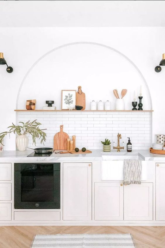 a modern kitchen with neutral base cabinets, white marble countertops, an arched niche with a tiled backsplash and an open shelf as decoration