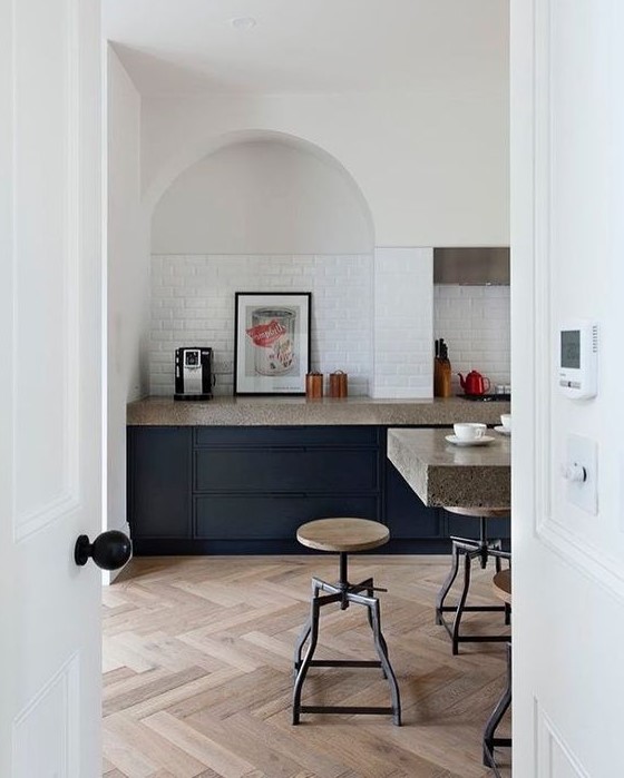 a modern kitchen with navy blue cabinets, gray granite countertops, and an arched alcove covered in tile and artwork