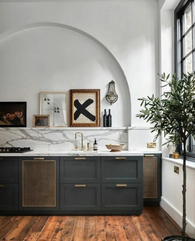 A stylish charcoal gray kitchen with a white marble backsplash and worktops, an arched niche with a mantel and a gallery wall within
