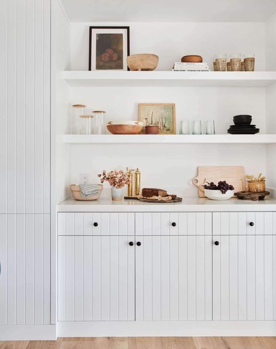 a white, modern farmhouse kitchen with a large alcove housing cabinets and open shelving that provide an alternative to an upper row of cabinets