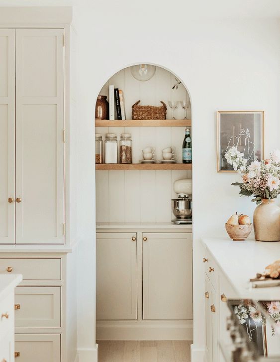 A white, modern farmhouse kitchen with an arched alcove that houses a pantry with shelves. A closet is a nice idea that saves space