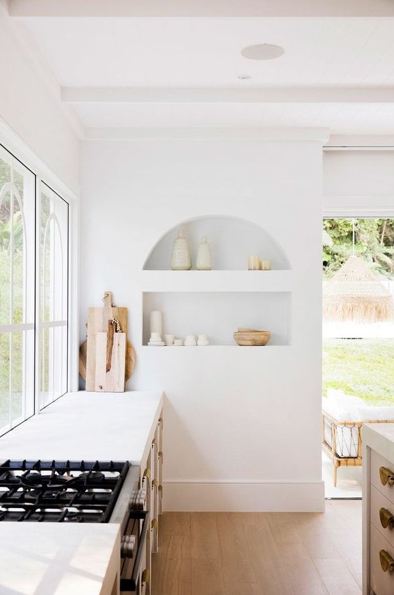 An airy white kitchen with an arched niche displaying beautiful tableware is a chic and beautiful space