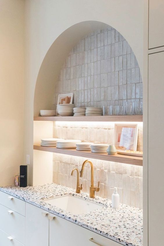 An arched niche covered with thin tiles, open illuminated shelves, china and glasses is a decorative and practical idea for a kitchen