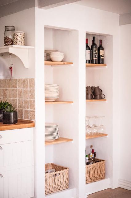 Tall niches with wooden shelves and baskets are used to store dishes, glasses and wine and are a great alternative to an upper row of cabinets