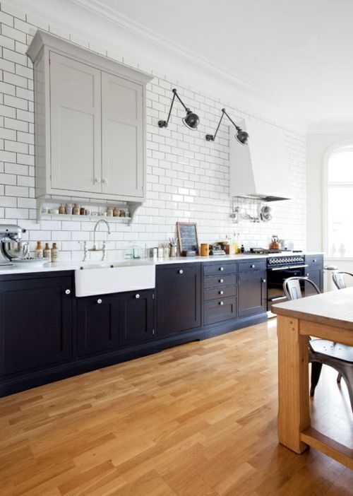 a beautiful kitchen with navy blue base cabinets, a gray upper cabinet, a white extractor hood and white subway tiles on the wall