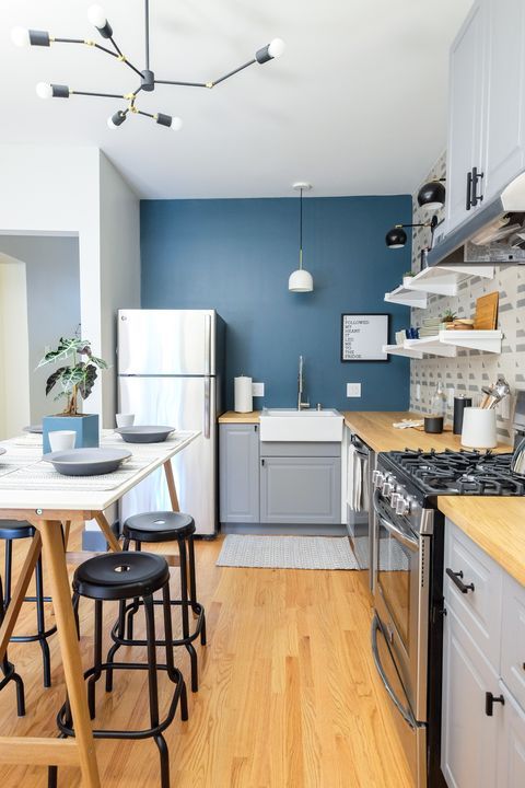 A chic and cool kitchen with a navy blue accent wall, gray cabinets, butcher block countertops, a trestle table and black stools