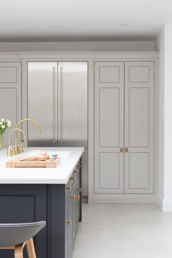 a sophisticated dove gray kitchen with shaker cabinets, a navy island, a white stone countertop and some gold knobs and pulls