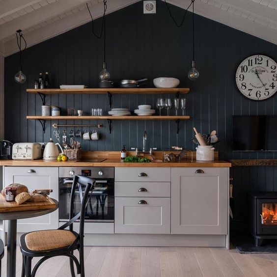 a small, pretty kitchen with gray cabinets, a navy blue accent wall, open shelving, butcher block countertops, and a small fireplace