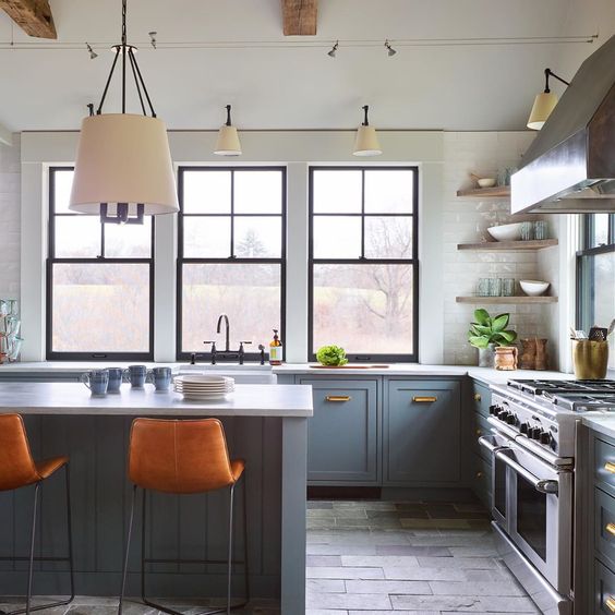 a stylish blue and gray kitchen with only base cabinets, corner shelves, a stove, a gray kitchen island and orange leather stools