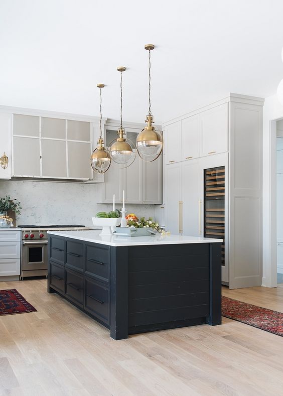 a stylish kitchen with white and dove gray cabinets, a midnight blue kitchen island and elegant gold pendant lamps