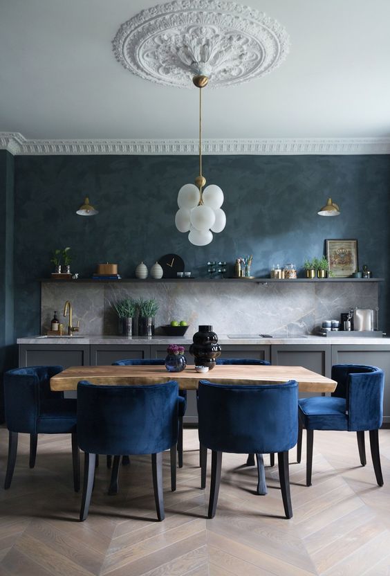 an exquisite kitchen with gray base cabinets, open shelving, gray stone backsplash and worktops, stained table and navy blue chairs