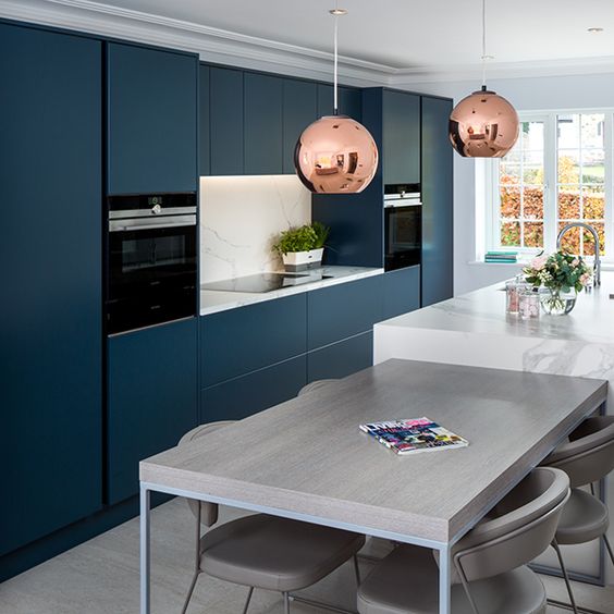 A chic modern navy blue kitchen with a white kitchen island and matching worktops and a gray table for breakfast