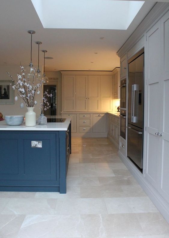 a dove gray kitchen with a bold blue island, white stone countertops and a neutral tile floor