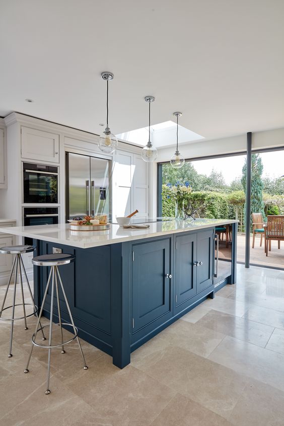 a dove gray kitchen with a large navy island and white stone countertops, as well as vintage stools and pendant lamps