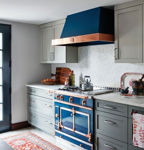 A gray Art Deco kitchen with a bright blue stove and copper accents and a mosaic tile backsplash looks stunning