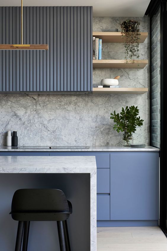 a minimalist blue kitchen with a gray stone backsplash and countertops, as well as potted plants and touches of gold