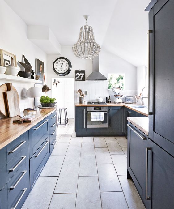 a navy blue kitchen with butcher block countertops, a gray tile floor, and a gray beaded chandelier for a bold touch