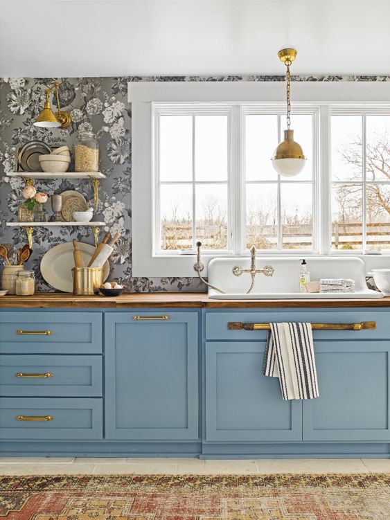 A pretty blue kitchen with a gray floral wallpaper and touches of gold and stained wood is vintage chic