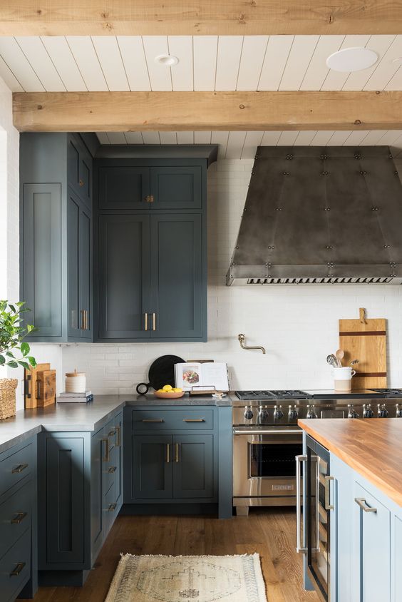A stylish blue kitchen with stainless steel appliances, natural wood accents, and brass is a super chic and cool space