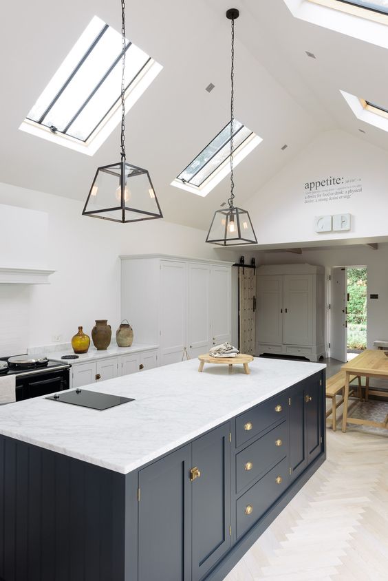 A stylish white kitchen with a Victorian feel and a navy blue kitchen island, skylights and pendant lamps accent the space
