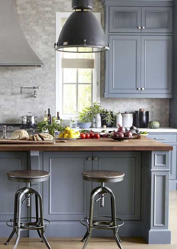 A traditional kitchen in slate blue with gray tiles, butcher block countertops and vintage furniture and lamps