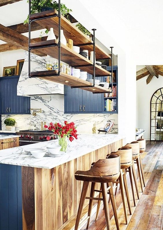 a beautiful kitchen with navy and stained cabinets, wooden beams, hanging shelves over the kitchen island and plywood stools