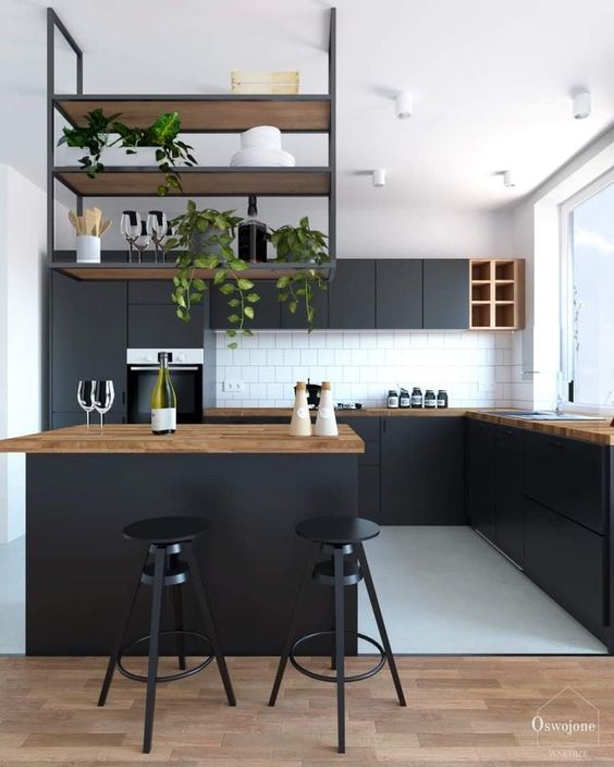 A modern black kitchen with butcher block countertops, a hanging shelf above the island and a white tile backsplash