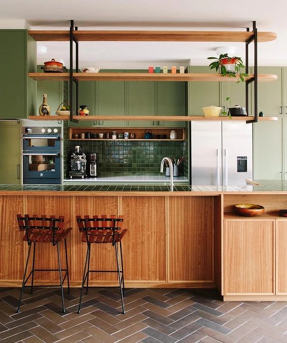 a green and stained kitchen with padded cabinets, hanging shelves above the kitchen island and wooden stools