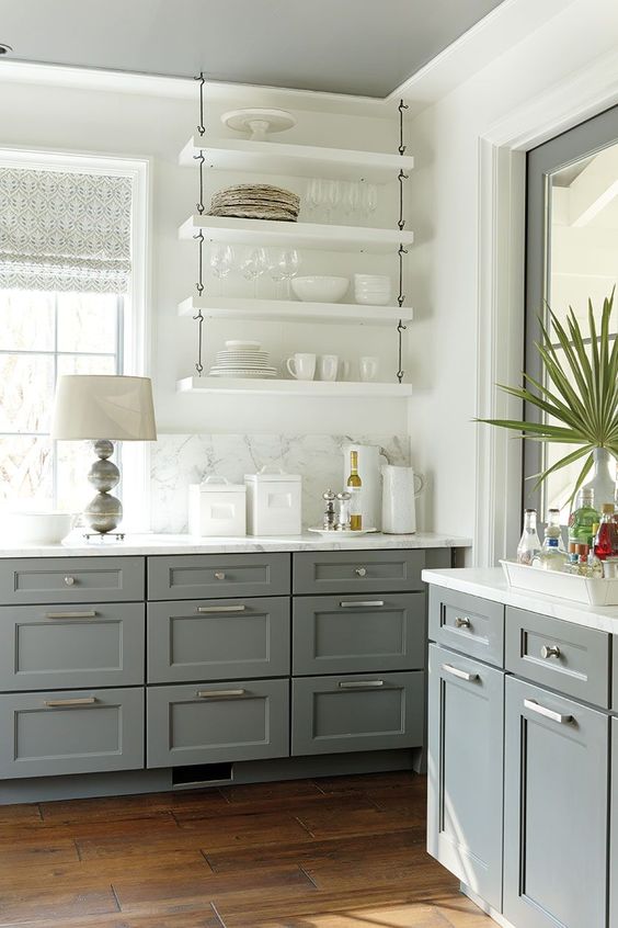 a gray-and-white farmhouse kitchen with shaker cabinets and white hanging shelves, a white marble backsplash and countertops