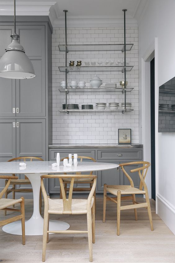 a gray farmhouse kitchen with a white subway tile backsplash, a hanging glass shelf, an oval table and stained chairs