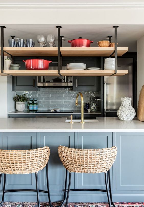 A light gray and graphite gray kitchen with a gray tile backsplash, hanging shelves, woven stools and brass and gold fixtures