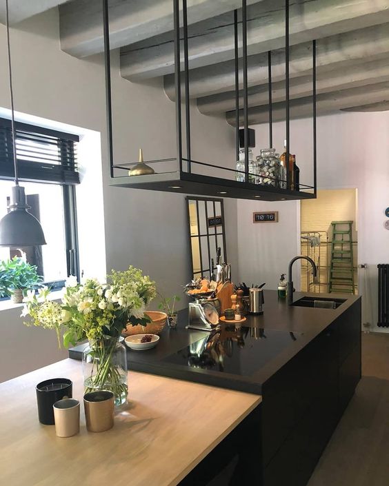 a minimalist kitchen with a black kitchen island and a black hanging shelf above it, with green plants and hanging lamps
