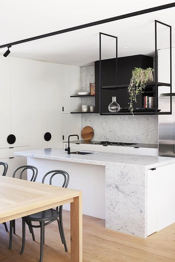 A modern black and white kitchen with white stone worktops and a splashback, a black hanging shelf and potted plants