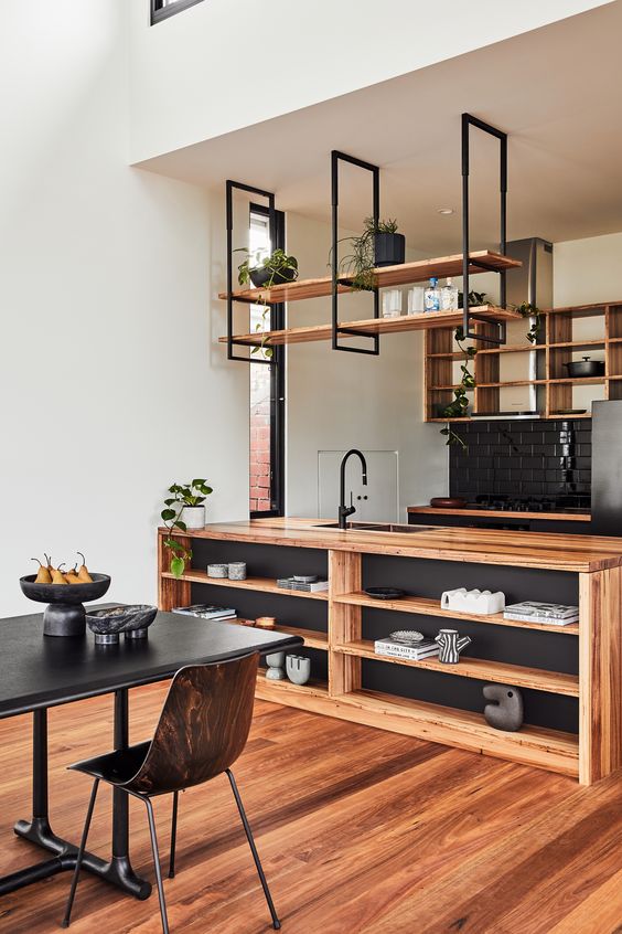 a stylish black and light stained wood kitchen with open cabinets and hanging shelves, a kitchen island and potted plants