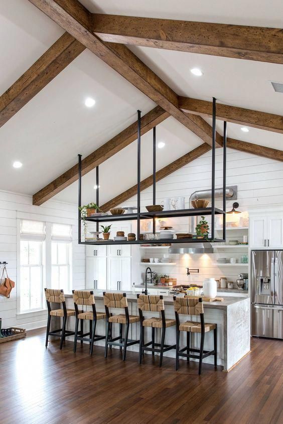A white, bead-clad country kitchen with molded cabinets, a large island and black hanging shelves above