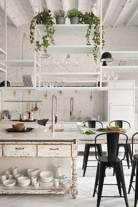 a white kitchen with modern cabinets and a shabby chic style kitchen island, hanging shelves and black metal chairs