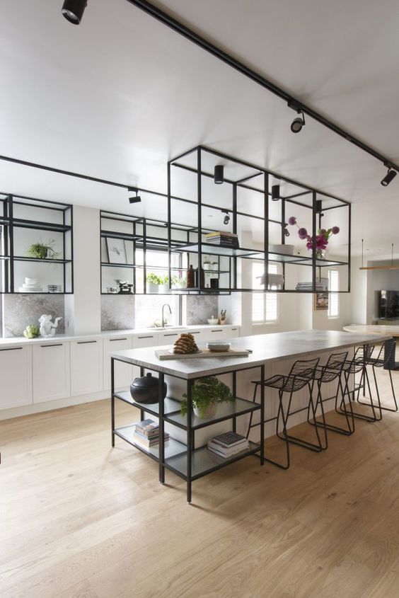 an airy kitchen with white cabinets and a large kitchen island, black metal and glass hanging shelves and black stools