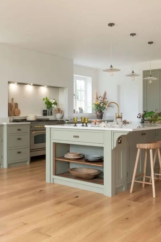 A chic sage green kitchen with separate cooking zone, flat panel cabinets, white stone countertops and brass fittings