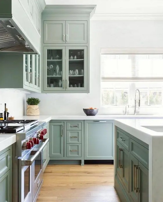 A classic shaker style kitchen in sage green with glass fronts, white stone worktops, backsplash and brass handles