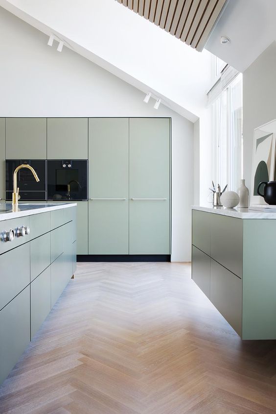 A minimalist sage green kitchen with flat cabinets, white stone countertops and gold fixtures is amazing